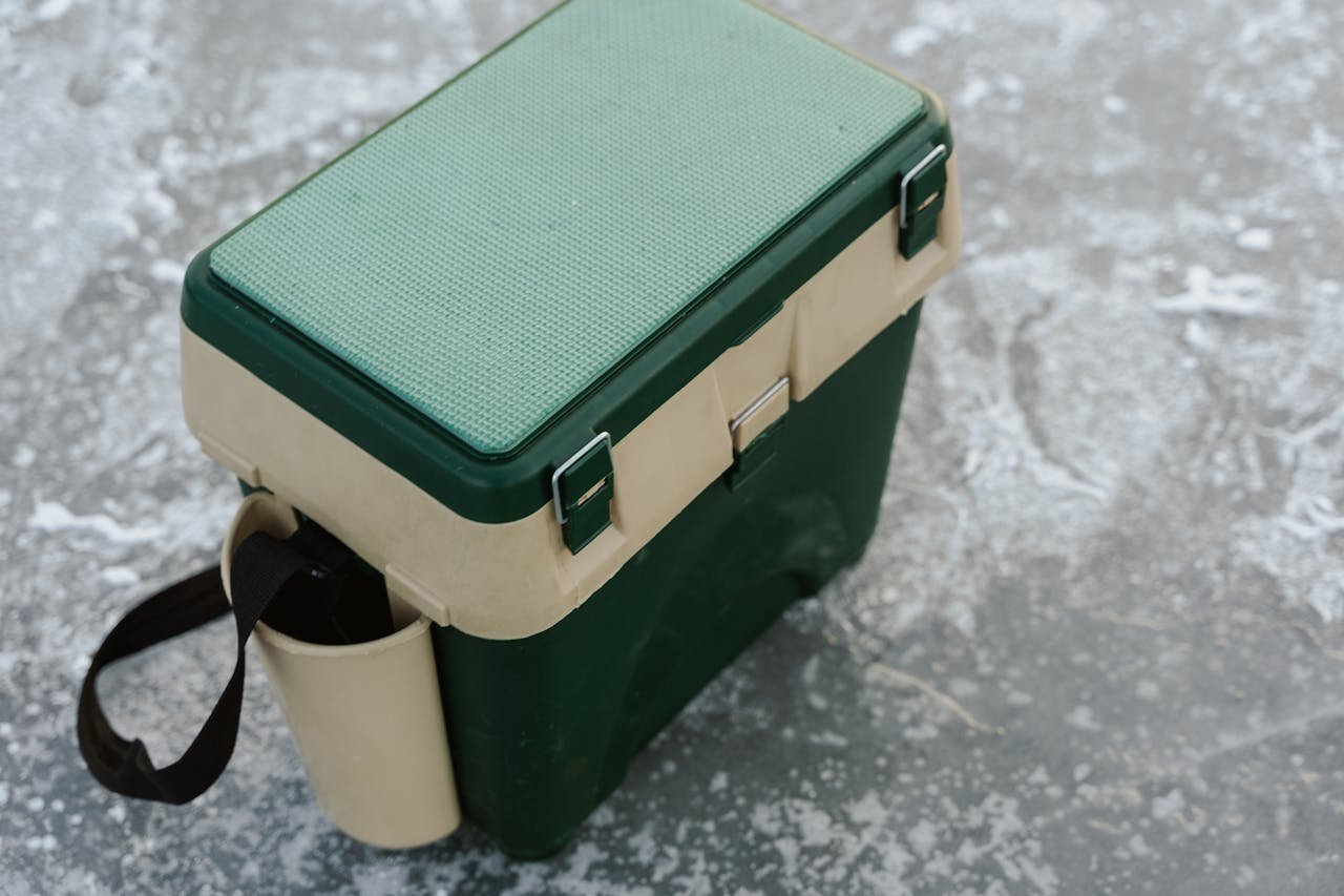 A green and beige cooler sits on a frozen ice surface, ideal for outdoor adventures.
